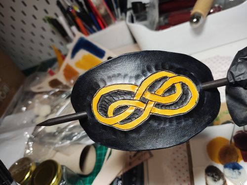 Black leather hairpin with a yellow infinite double loop and with a black wooded stick to attach to the hairs.