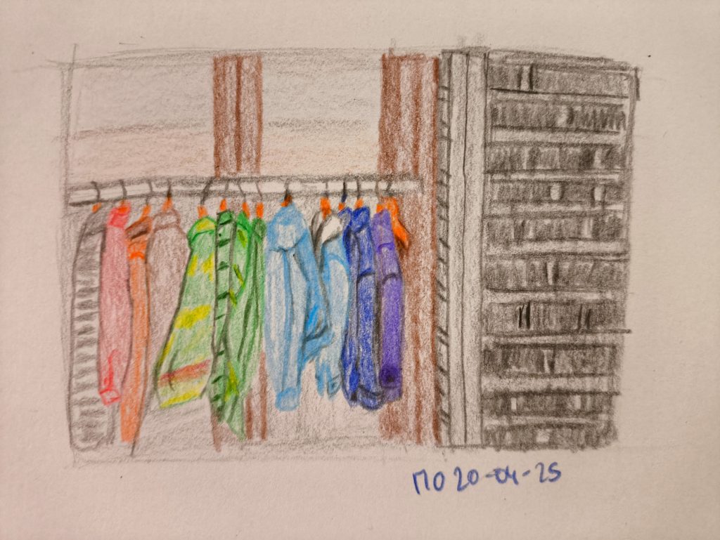 Various colored clothes and jackets on a rack in front of a window of an outfit or second hand shops.